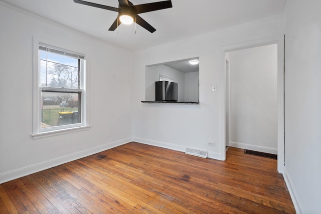 empty room with wood-type flooring, visible vents, baseboards, and a ceiling fan