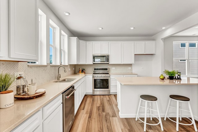 kitchen featuring light wood-style flooring, appliances with stainless steel finishes, white cabinetry, a sink, and a kitchen breakfast bar