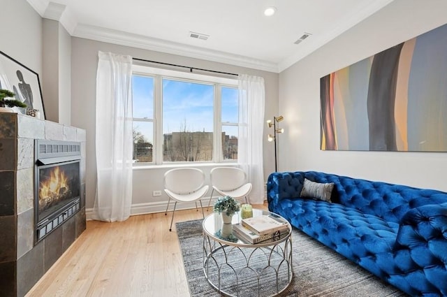 living area with ornamental molding, a tile fireplace, baseboards, and wood finished floors