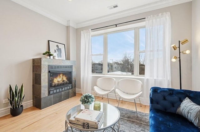 sitting room with crown molding, visible vents, wood finished floors, a tile fireplace, and baseboards