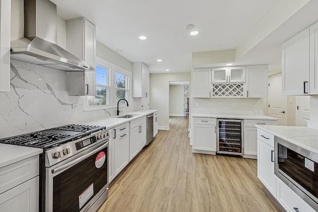 kitchen featuring beverage cooler, light wood-type flooring, stainless steel appliances, wall chimney exhaust hood, and a sink