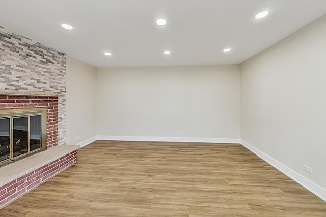 unfurnished living room featuring recessed lighting, a fireplace, baseboards, and wood finished floors