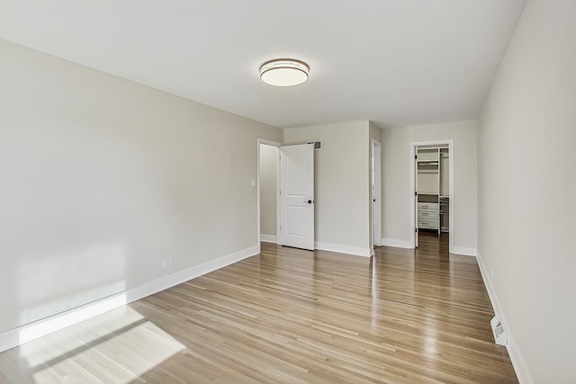 unfurnished bedroom featuring a spacious closet, light wood-style floors, and baseboards