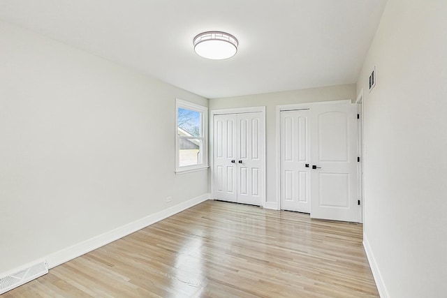 unfurnished bedroom featuring visible vents, light wood-style flooring, two closets, and baseboards