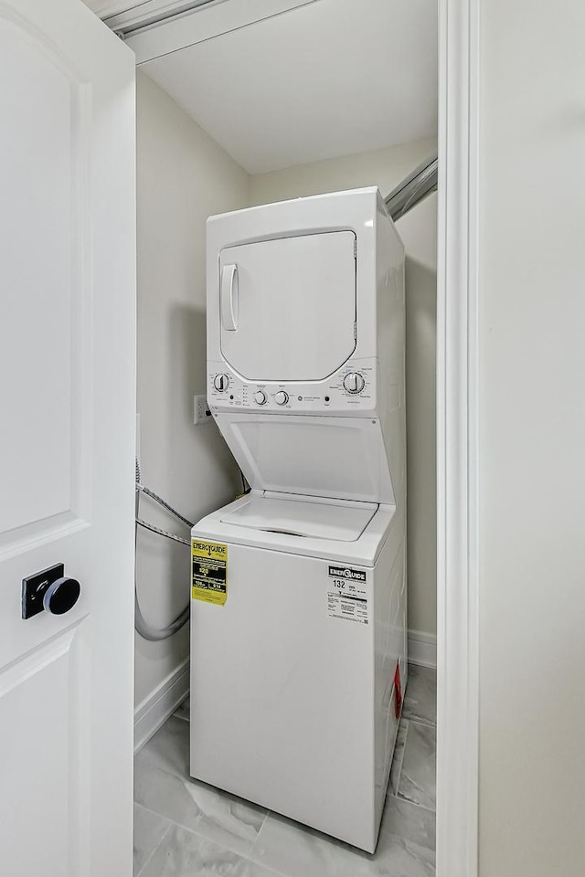 laundry room featuring stacked washer / dryer, marble finish floor, laundry area, and baseboards