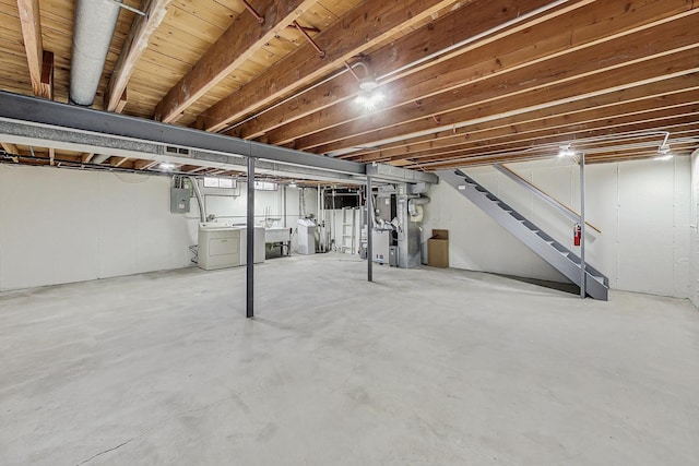 unfinished below grade area featuring heating unit, stairway, electric panel, and separate washer and dryer