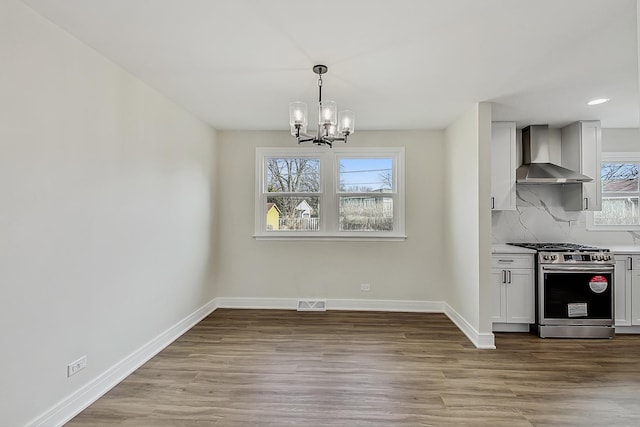 kitchen featuring visible vents, baseboards, stainless steel range with gas stovetop, wall chimney range hood, and backsplash