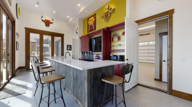 kitchen featuring recessed lighting, a towering ceiling, light countertops, french doors, and a kitchen bar