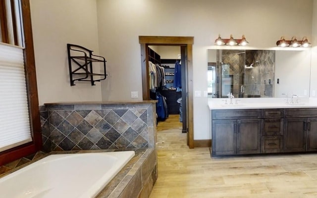 bathroom featuring double vanity, wood finished floors, a sink, a shower stall, and a bath