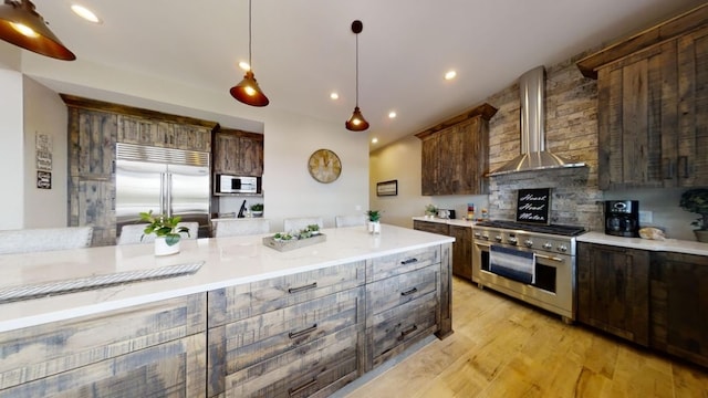 kitchen with recessed lighting, light wood-style flooring, dark brown cabinets, high quality appliances, and wall chimney exhaust hood