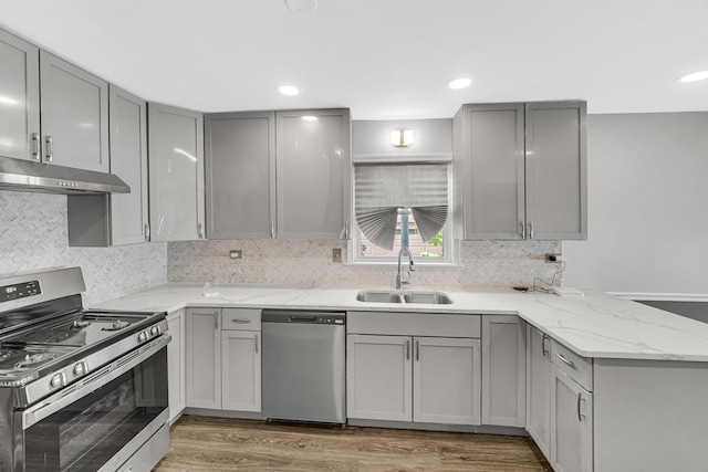 kitchen with stainless steel appliances, under cabinet range hood, a sink, and gray cabinetry