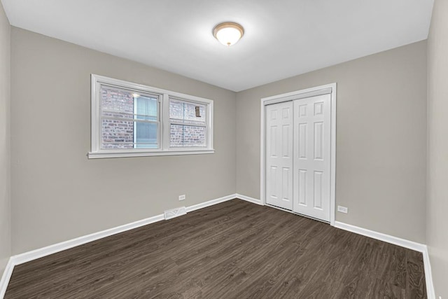 unfurnished bedroom featuring visible vents, baseboards, dark wood finished floors, and a closet