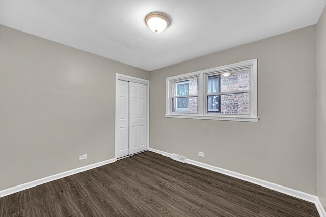 unfurnished bedroom with dark wood-type flooring, a closet, visible vents, and baseboards