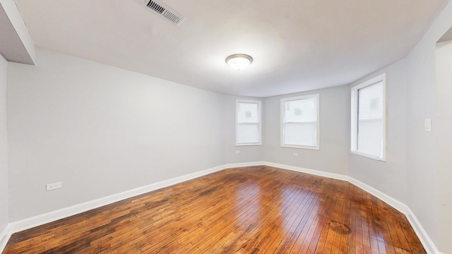 spare room featuring dark wood-type flooring, visible vents, and baseboards