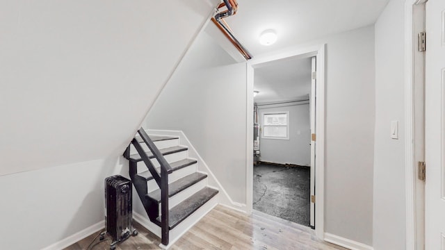 staircase with radiator heating unit, wood finished floors, and baseboards