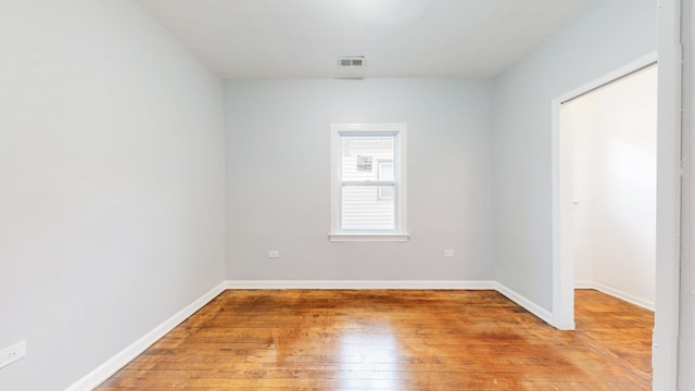 empty room with light wood finished floors, visible vents, and baseboards