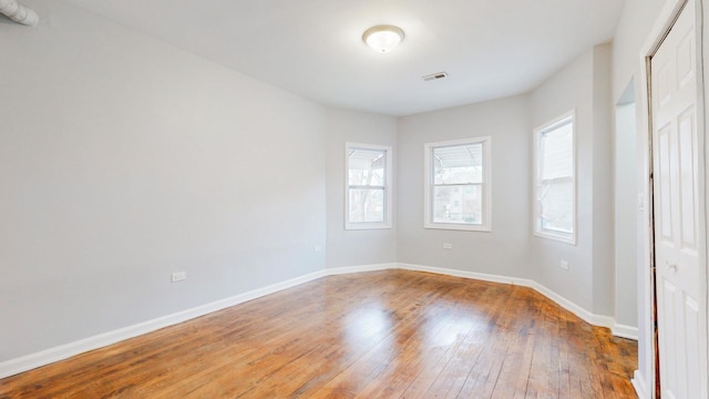 spare room with wood-type flooring, visible vents, and baseboards