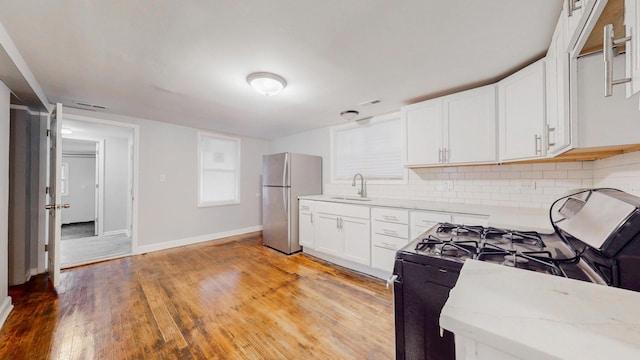 kitchen with range with gas stovetop, light wood finished floors, tasteful backsplash, freestanding refrigerator, and white cabinetry