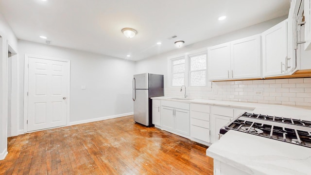 kitchen featuring freestanding refrigerator, a sink, light wood-style floors, white cabinetry, and backsplash