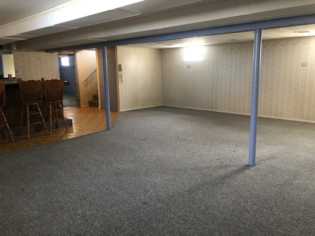 below grade area featuring carpet, a dry bar, stairway, baseboards, and wallpapered walls