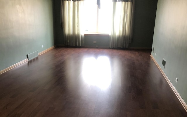 spare room featuring baseboards, visible vents, and dark wood-style flooring