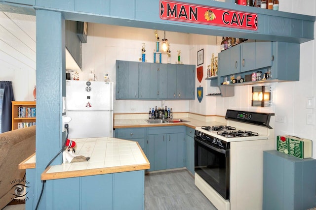 kitchen with tile countertops, blue cabinets, freestanding refrigerator, and range with gas stovetop