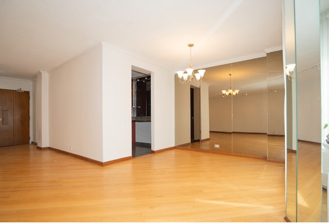 unfurnished room featuring baseboards, light wood finished floors, ornamental molding, and an inviting chandelier