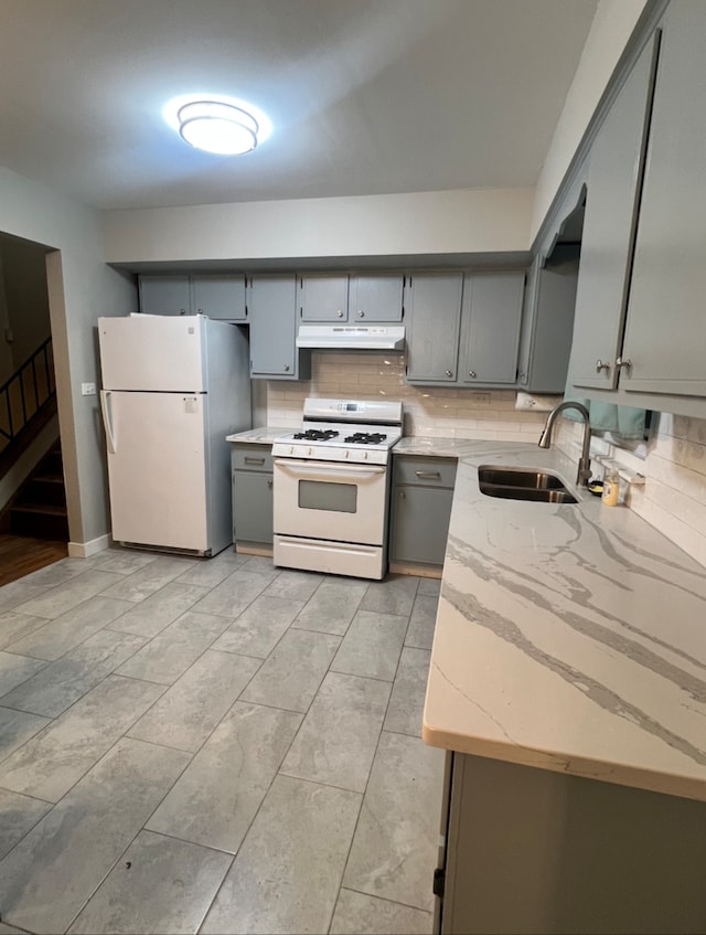 kitchen featuring gray cabinets, a sink, under cabinet range hood, white appliances, and decorative backsplash