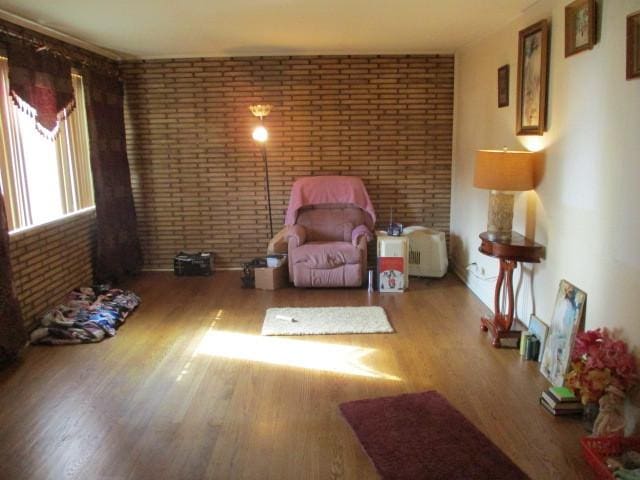 living area with brick wall and wood finished floors