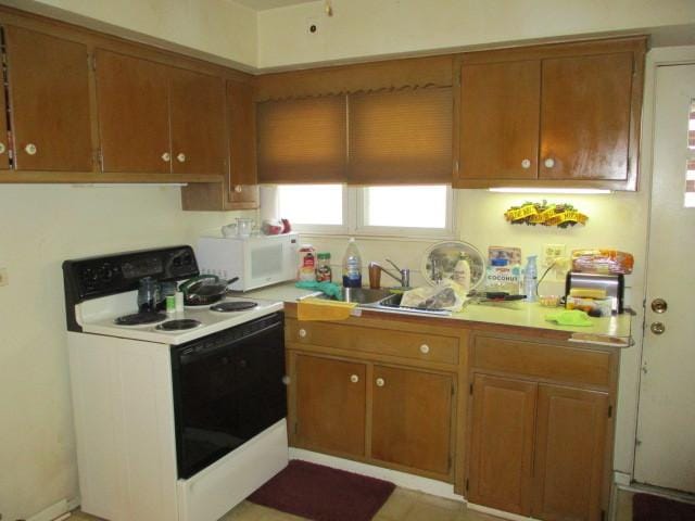 kitchen featuring electric range oven, light countertops, white microwave, and brown cabinetry