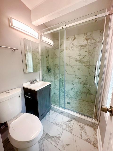 bathroom featuring marble finish floor, vanity, toilet, and a shower stall