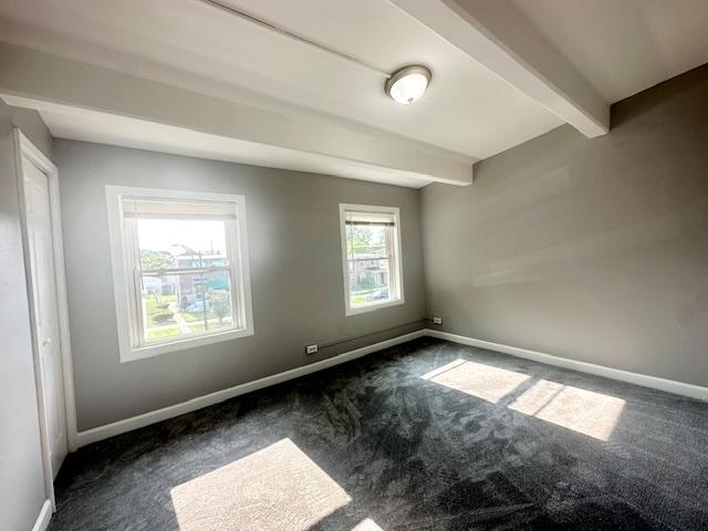 empty room with beamed ceiling, carpet flooring, and baseboards