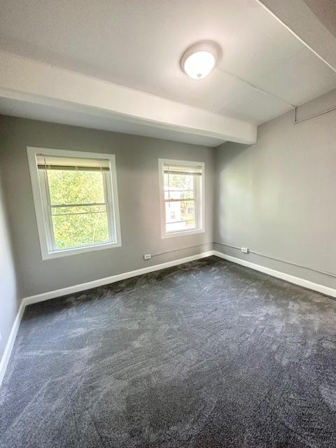 unfurnished room with beam ceiling, dark carpet, and baseboards