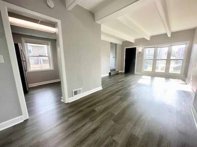 unfurnished living room featuring dark wood-style floors, visible vents, beam ceiling, and baseboards