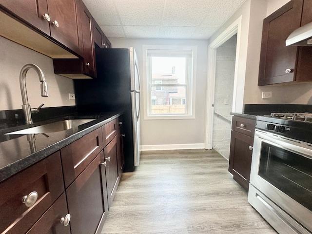 kitchen with dark brown cabinetry, gas range, light wood-style flooring, under cabinet range hood, and a sink