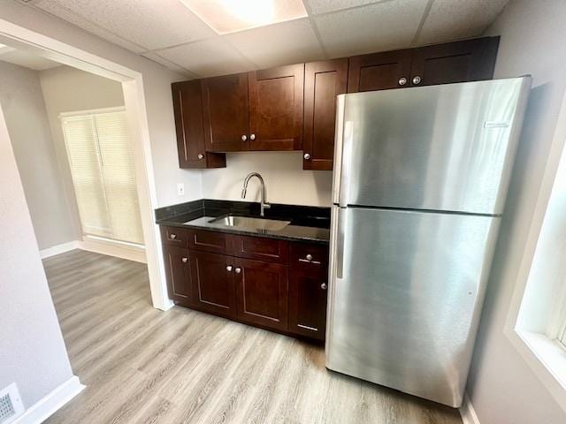 kitchen with a drop ceiling, light wood-style flooring, a sink, freestanding refrigerator, and dark countertops