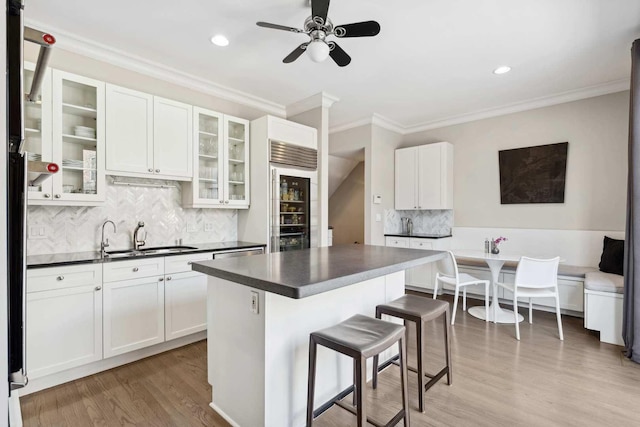 kitchen featuring a breakfast bar, dark countertops, light wood-style floors, white cabinetry, and a sink