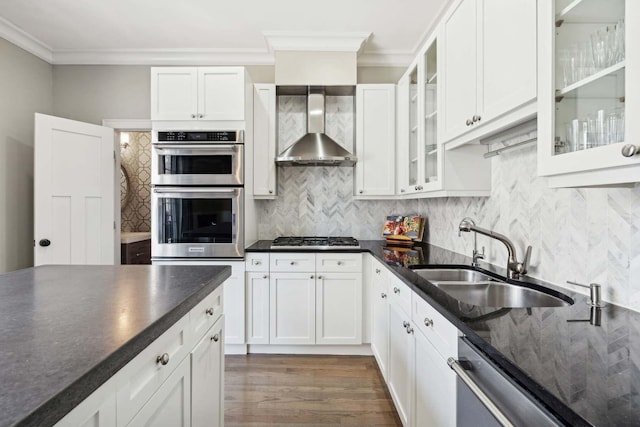 kitchen with decorative backsplash, stainless steel appliances, crown molding, wall chimney range hood, and a sink