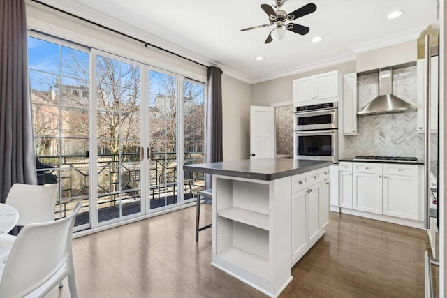 kitchen with open shelves, dark countertops, backsplash, stainless steel double oven, and wall chimney range hood