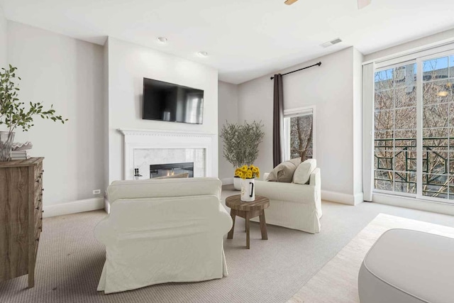 living room with baseboards, a glass covered fireplace, visible vents, and light colored carpet