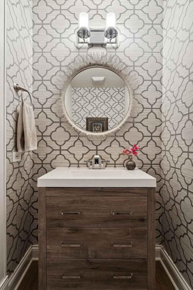 bathroom featuring wallpapered walls, baseboards, and vanity