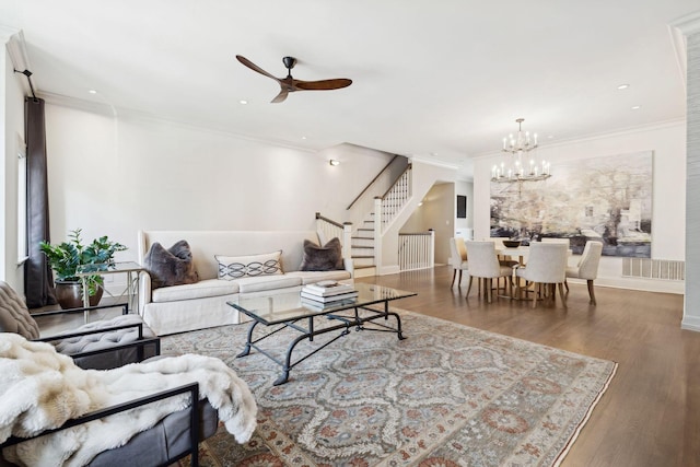 living area with ceiling fan with notable chandelier, crown molding, stairway, and wood finished floors