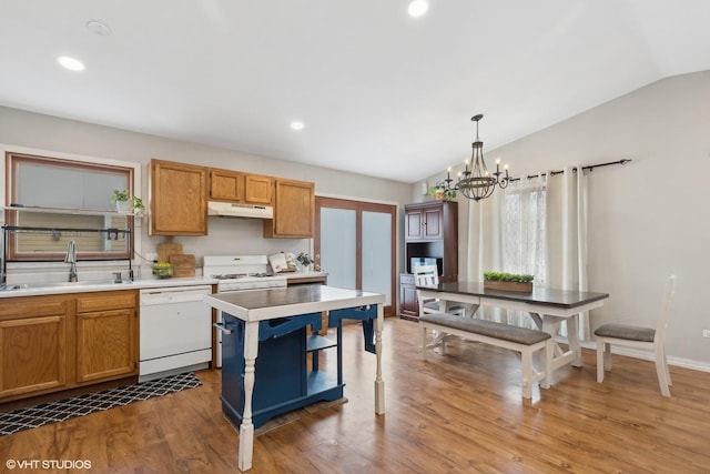 kitchen with under cabinet range hood, white appliances, wood finished floors, a sink, and vaulted ceiling