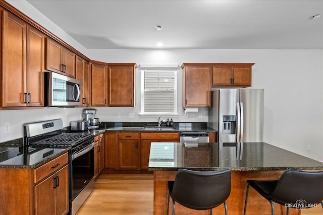 kitchen featuring dark stone counters, appliances with stainless steel finishes, a breakfast bar, light wood-style floors, and a sink