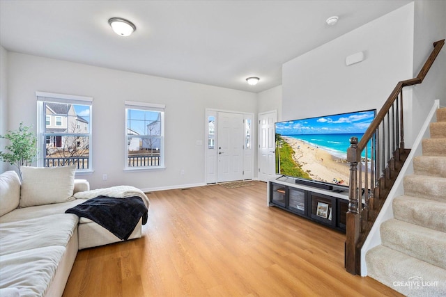 living area with light wood-type flooring, stairway, and baseboards