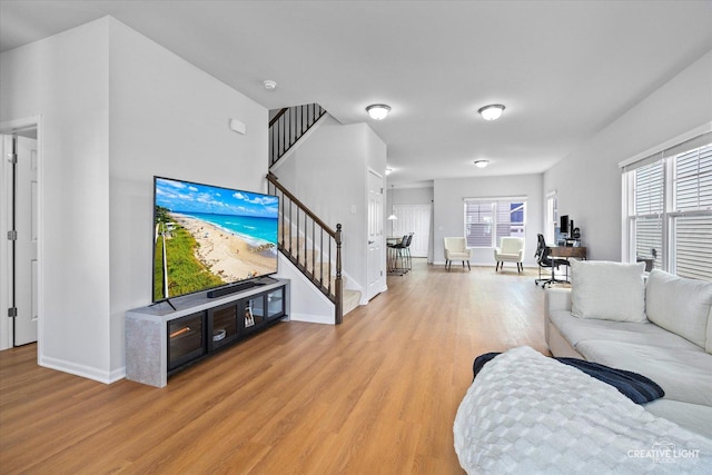 living room with a wealth of natural light, stairway, light wood-style flooring, and baseboards