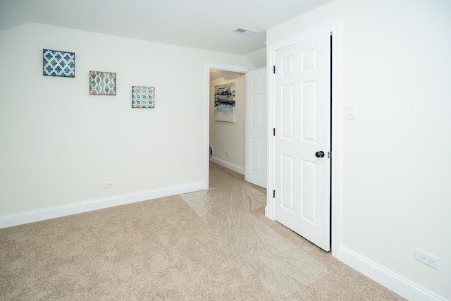 unfurnished bedroom featuring light colored carpet, vaulted ceiling, visible vents, and baseboards