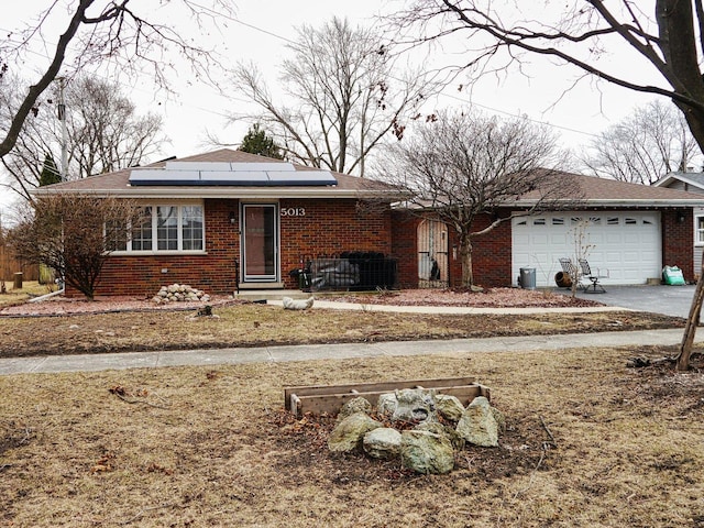 view of front of home featuring a garage, brick siding, driveway, and solar panels