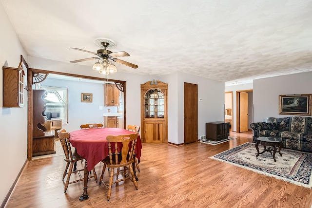 dining space with ceiling fan, light wood finished floors, a textured ceiling, and baseboards