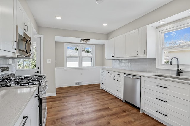 kitchen with visible vents, light wood-style flooring, a sink, appliances with stainless steel finishes, and decorative backsplash